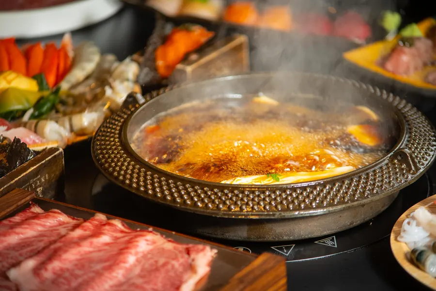 The sukiyaki pot bubbling beside a plate of wagyu